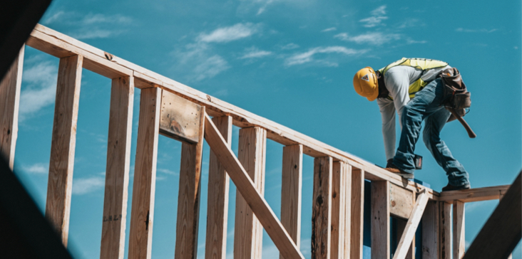 A man holding a yellow hard hat on top of a wooden structure.