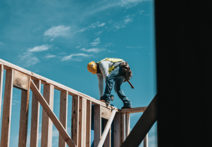 A construction worker is climbing up the side of a building.